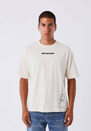 Camiseta de manga corta color crema con un logo negro "PXP", que cuenta con un patrón texturizado en la parte inferior izquierda en tonos gris y púrpura.