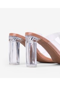 Las sandalias de tacón transparente cuentan con una base de color durazno, tiras transparentes y tacones claros en bloque. El diseño es moderno y minimalista.