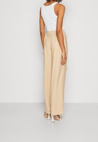 Beige brede broekspijpen gemaakt van een gladde stof, met een hoge taille en koordceintuur, gecombineerd met een wit tanktopje.