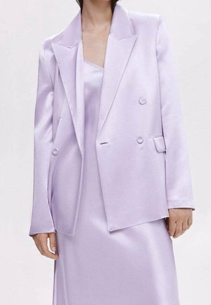 Frau trägt ein helllila Satinschlüpferkleid und einen passenden zweireihigen Blazer mit Knöpfen und gekerbtem Revers.