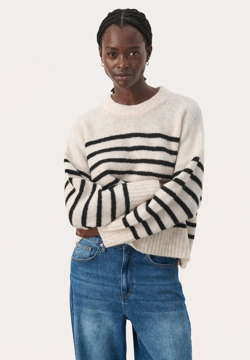 Maglione a righe crema e nero con collo e polsini a costine, indossato con jeans azzurri chiari; tessuto a maglia morbida e testurizzata.