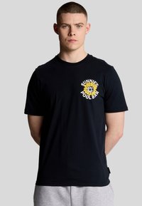 Sort bomulds t-shirt med et solsikke grafisk design iført solbriller og teksten "SUNNIES POOL BAR" i hvid, rund halsudskæring, korte ærmer.
