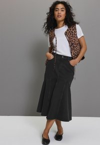 Čierna riflová sukňa s rozšíreným strihom a vreckami, v kombinácii s bielym tričkom a hnedou vestou s leopardím vzorom. Čierne baleríny dotvárajú outfit.