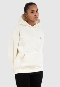 Hoodie in Creme, aus weichem Stoff gefertigt. Verfügt über eine Kängurutasche und gerippten Saum. Mit einem kleinen dekorativen Design auf der Brust akzentuiert.