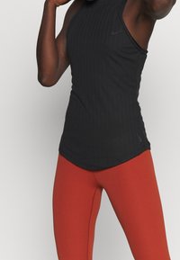 Débardeur de sport noir à côtes avec un col montant, associé à un legging rouge moulant ; tous deux fabriqués dans un matériau extensible et respirant.