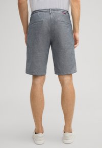 Graue Shorts mit feiner Textur, entspannter Passform, zwei Gesäßtaschen und einem elastischen Bund. Getragen mit weißen Sportschuhen.