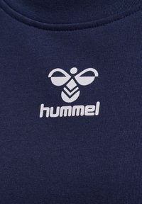 Pull-over navy avec une texture douce, arborant un logo Hummel blanc et un design d'abeille sur le devant. Col rond avec une finition sans couture.