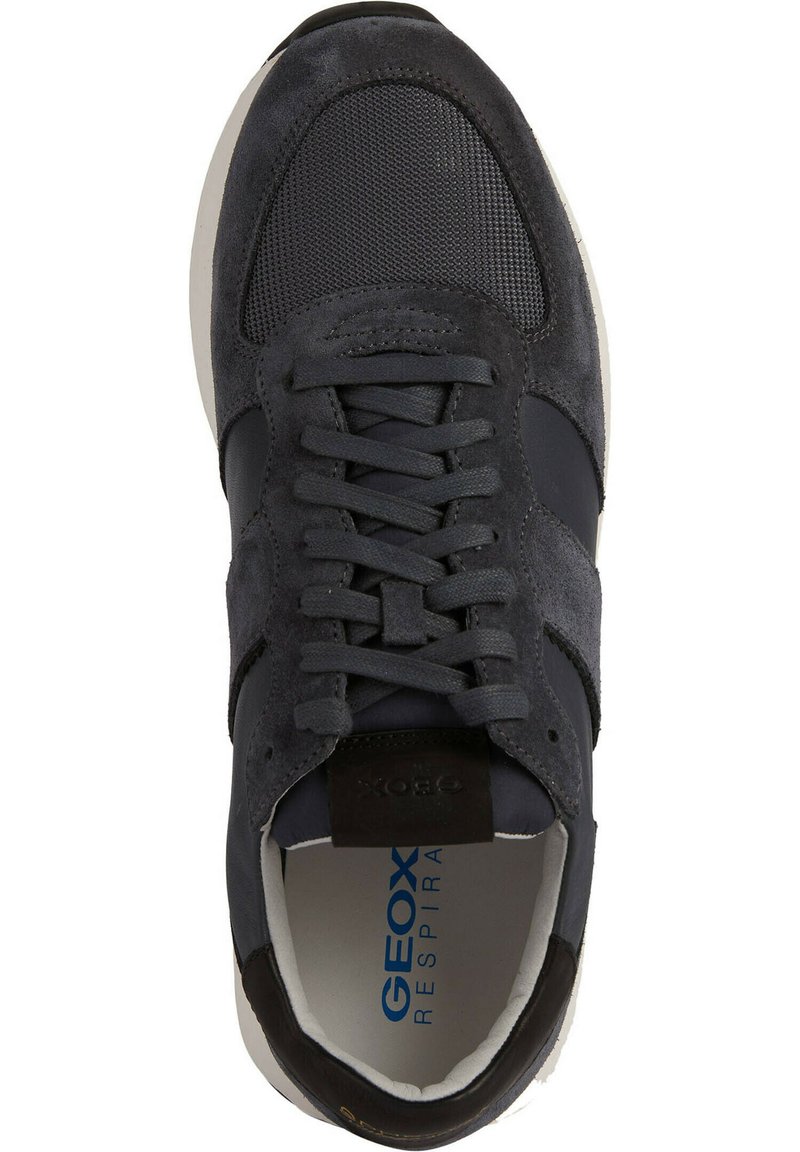 Sneaker in suede e mesh grigio scuro con chiusura a lacci, suola bianca e dettagli con logo. Presenta una superficie testurizzata e un accento a contrasto.