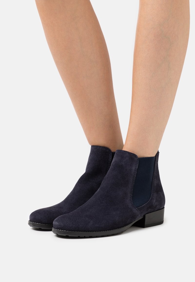 Stivaletti Chelsea in suede blu navy al polpaccio, con pannelli elastici neri sui lati e tacco basso, indossati su gambe nude contro uno sfondo bianco.
