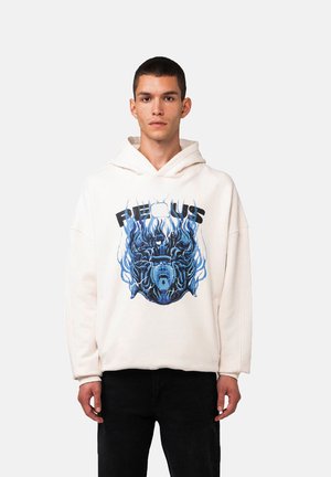 Felpa crema con un design grafico che presenta un volto illustrato blu e nero circondato da fiamme. Materiale in cotone, vestibilità rilassata e tasca a marsupio.