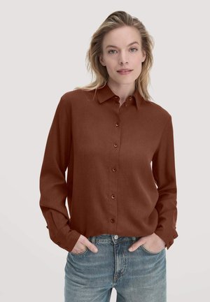 Brown button-up shirt made of smooth fabric, featuring a classic collar and long sleeves, paired with light blue jeans.