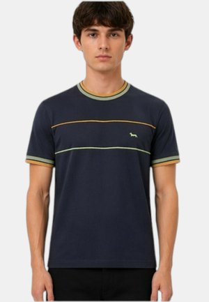 Giovane uomo che indossa una maglietta blu navy con strisce gialle e verdi sul petto e colletto e bordi delle maniche abbinati.