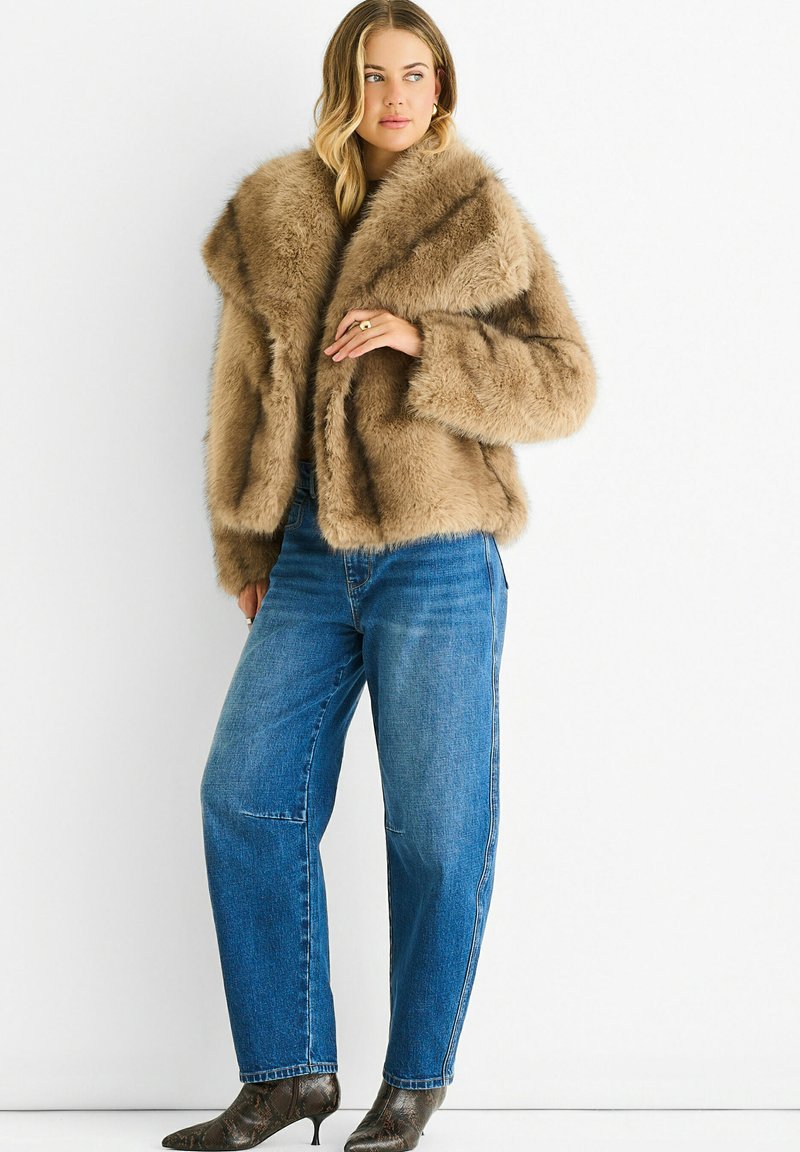 Brown faux fur cropped jacket with a broad collar, fluffy texture, and loose fit, paired with high-waisted blue denim jeans and patterned heels.