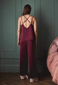 Set de camisolă și pantaloni din satin burgund. Camisola are un spate în formă de V și bretele încrucișate. Pantalonii au accente de dantelă la tiv. Textură fină.