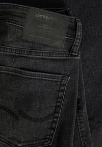 Jeans din denim negru cu o suprafață texturată, având o etichetă cu "JACK & JONES" și "JEANS INTELLIGENCE." Design clasic cu cinci buzunare.