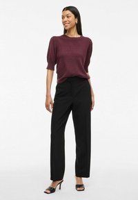 Haut en tricot bordeaux à manches courtes bouffantes, associé à un pantalon noir taille haute et des sandales à talons ouverts noires. Texture lisse.
