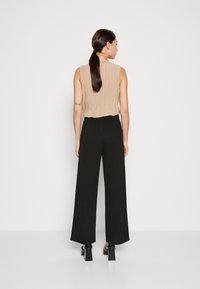 Haut sans manches plissé beige associé à un pantalon large noir. Le pantalon a une taille élastique et est porté avec des chaussures à talons blocs.