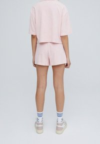Cropped shirt a maniche corte rosa chiaro abbinato a pantaloni corti a vita alta dello stesso colore. Scarpe bianche di base con dettagli rosa e calze a righe blu.