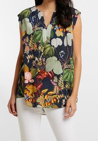 Blusa con stampa floreale, maniche corte, scollatura a V e orlo curvo. Presenta colori vivaci su uno sfondo scuro, realizzata in tessuto leggero.