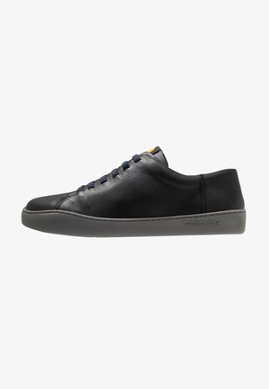 Black leather sneaker with a smooth texture, round toe, navy laces, and a gray rubber sole featuring the brand name "camper."