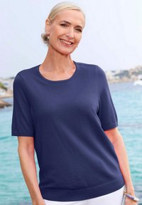 Marineblaues kurzärmliges Strickoberteil mit rundem Ausschnitt, gerippter Textur und Hüftlänge, kombiniert mit weißen Hosen.