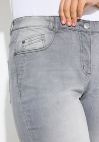 Jeans in denim grigio con una leggera scoloritura, caratterizzati da un classico design a cinque tasche, bottone in metallo e dettagli ricamati lungo le cuciture.