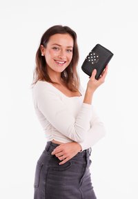 Black wallet with a textured surface and polka dot accent; model showing wallet with a white long-sleeve top and gray skirt.