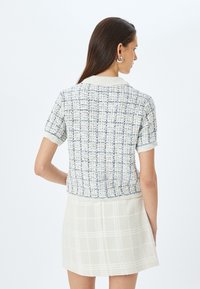 Korte mouwen gebreide top in crème en marineblauw met een textuurpatroon, voorzien van een geribbelde kraag en manchetten. Draagt met een crème rok.