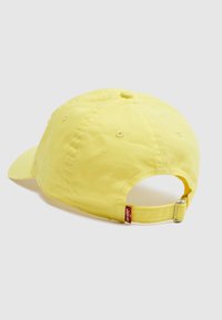 Κίτρινο βαμβακερό καπέλο μπέιζμπολ με ρυθμιζόμενο ιμάντα και μεταλλική αγκράφα, που δείχνει την πίσω όψη σε ανοιχτό γκρι φόντο.