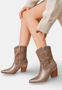 Bottes de cowboy marron de longueur cheville, fabriquées à partir d'un mélange de daim et de matériau métallique. Présentent un bout pointu, des broderies florales et un talon carré.