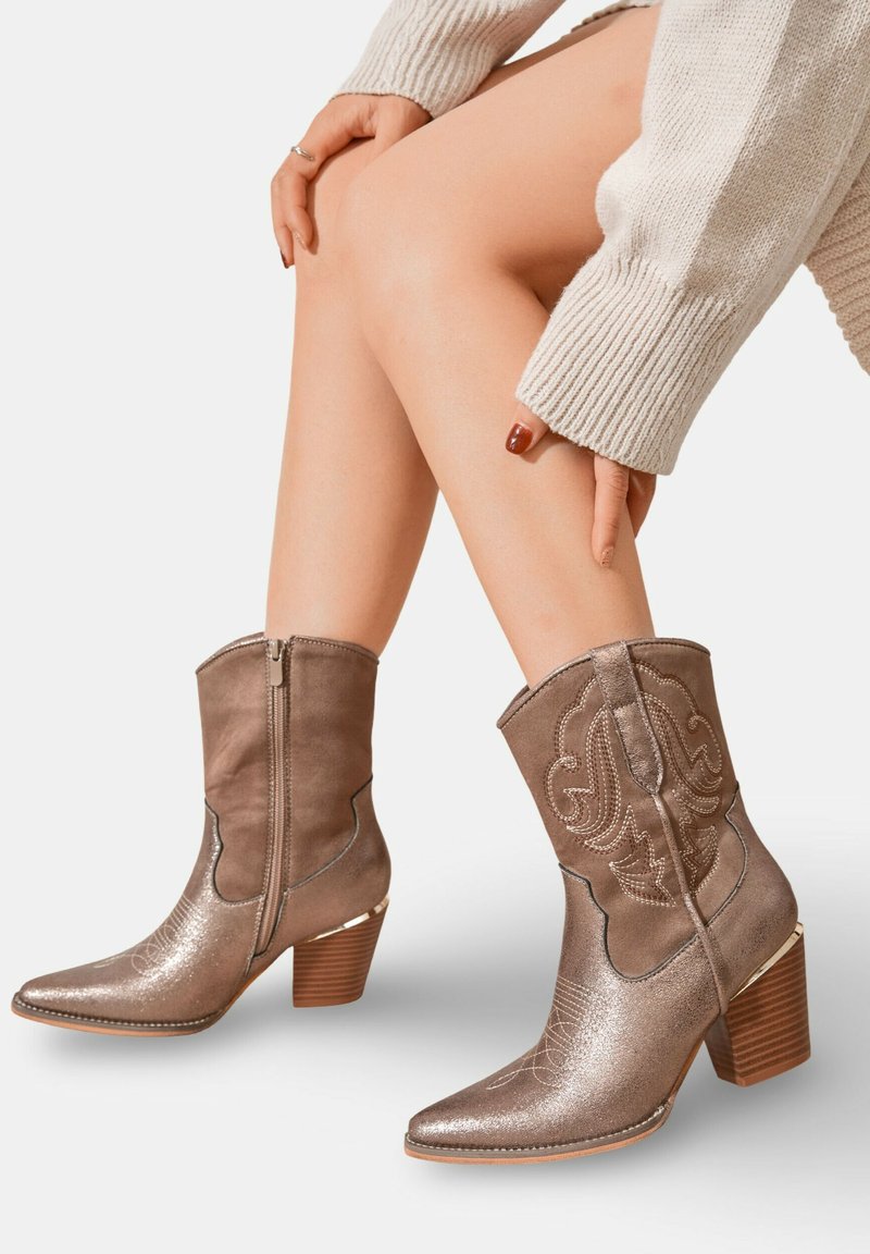 Bottes de cowboy marron de longueur cheville, fabriquées à partir d'un mélange de daim et de matériau métallique. Présentent un bout pointu, des broderies florales et un talon carré.