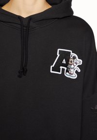 Black hooded sweatshirt featuring an embroidered letter "A" and a cartoon character, complemented by drawstrings and a smooth texture.