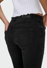 Mustad teksapüksid, mis on valmistatud denimist, istuva lõikega, viie tasku stiilis ja õrnalt nähtava brändi sildiga vöökohal.