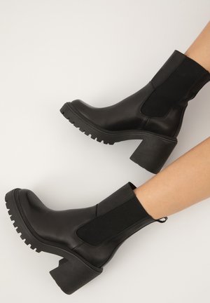 Botines negros de piel con paneles laterales elásticos, tacones gruesos y suelas de goma antideslizantes. Acabado suave con un diseño moderno.
