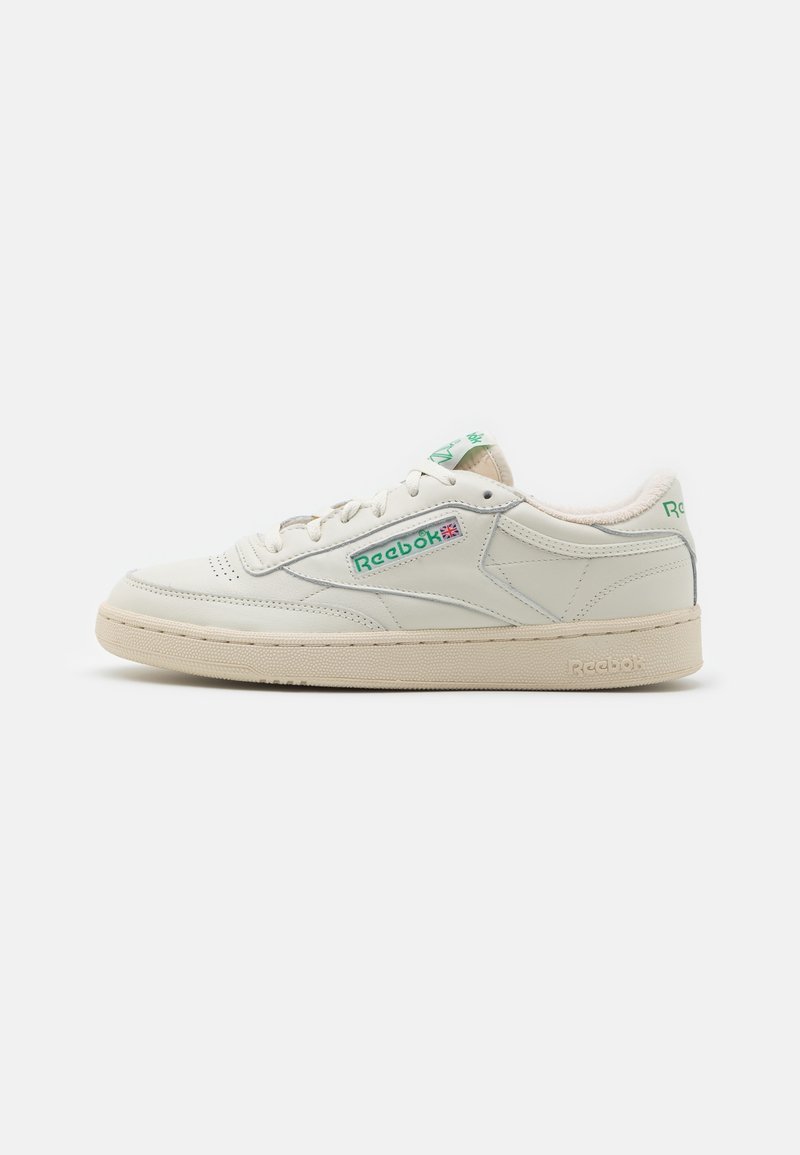White low-top Reebok sneaker with green logo accents, stitched panel design, and beige rubber sole shown in side profile on plain background.