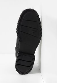 Suela negra de zapato con surcos profundos, hecha de goma. Presenta una base plana con líneas horizontales y acentos en las esquinas. Marcada con "CAMPER 42."