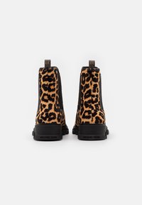 Une paire de bottines à imprimé léopard Michael Kors avec des semelles noires épaisses, vues de l'arrière sur un fond blanc uni.