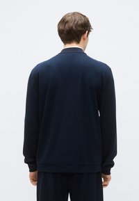 Felpa blu navy a maniche lunghe con collo e polsini a costine, texture liscia e vestibilità comoda, vista da dietro.