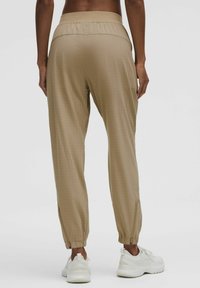 Beige, lightweight joggers with a stretchy waistband, tapered cuffs, and subtle perforated texture. Paired with white athletic shoes.