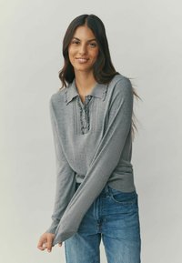 Gray long-sleeve sweater with a collar, featuring a button placket and ruffle detailing. Soft texture, paired with blue jeans.