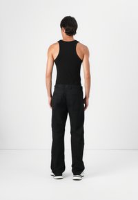Black tank top and dark trousers, with a relaxed fit. The fabric appears smooth, and the design is unembellished with standard stitching.