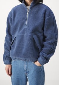 Mörkblå fleecepullover med kvartdragkedja, texturerad yta och elastiska ärmslut; har sidofickor och släta tygdetaljer.