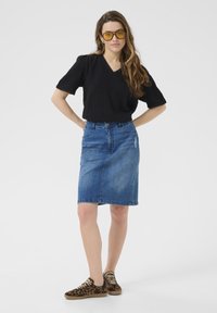 Sort tekstureret top med korte ærmer, blå denim kneelængde nederdel, leopardmønstret sneakers, rimløse gule solbriller. Enkel og afslappet design.