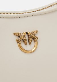 White leather handbag featuring a gold-tone metal clasp with two bird designs. Smooth texture with visible stitching along the zipper.