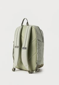 Πράσινο καμβά σακίδιο με επενδυμένους ιμάντες, διακοσμητική ραφή σε σχήμα ρόμβου, ετικέτα με λογότυπο και πλαϊνές τσέπες, με αεροδυναμικό ορθογώνιο σχήμα.