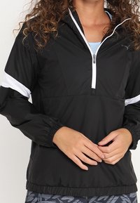 Czarna lekka kurtka z białymi paskami, z półzamkiem z przodu, elastycznymi mankietami i luźnym krojem, wykonana z gładkiego, wodoodpornego materiału.