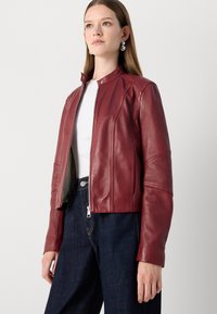 Bordo usnjeni jopič z zadrgo spredaj, podaljšanim ovratnikom in podrobnostmi ob straneh, v kombinaciji s temno jeans tkanino. Gladka tekstura in prilagojen kroj.