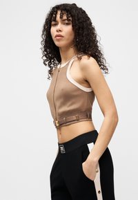 Καφέ κοντό τοπ με φερμουάρ στο μπροστινό μέρος, κρεμ τιράντες στους ώμους και εφαρμοστή γραμμή, με λεπτομέρεια ζώνης και μεταλλικά στοιχεία σε χρυσό τόνο.