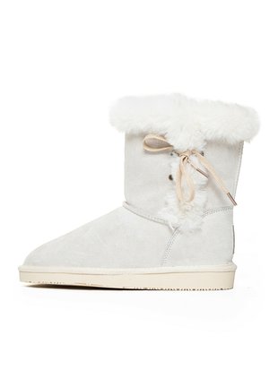 White suede ankle boot featuring a faux fur top cuff and a lace-up detail on the side. The sole is beige with textured grip patterns.