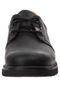 Scarpa in pelle nera con texture liscia, punta arrotondata e design con lacci. Presenta una suola nera robusta e un accento tan discreto all'interno.